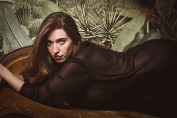 Reclining across a velvet chaise in a sheer black robe, botanical wallpaper behind