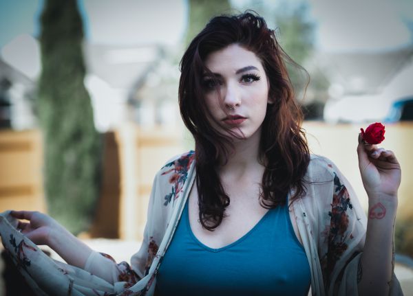 Outdoor portrait in a teal tank top and floral kimono, holding a small red rose