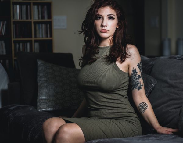 Seated on a dark sofa in an olive ribbed dress, one arm resting along the cushions
